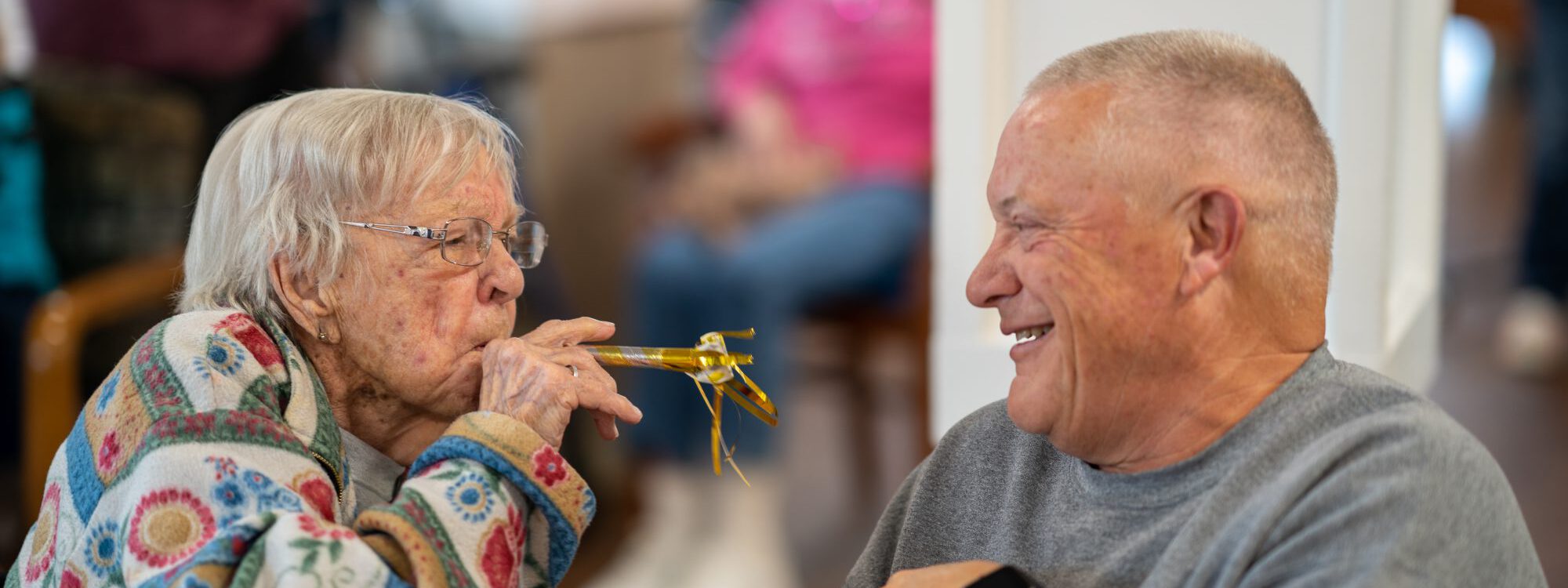 A woman blowing a party horn at a man while he laughs