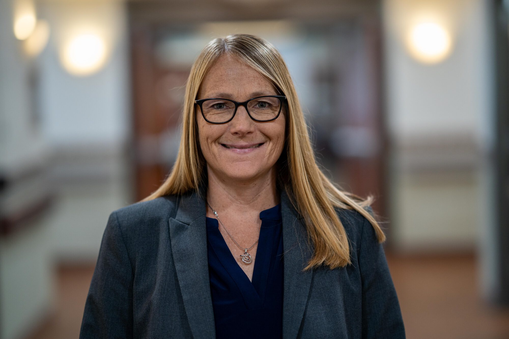 head shot of woman in a navy blue blazer wearing black glasses